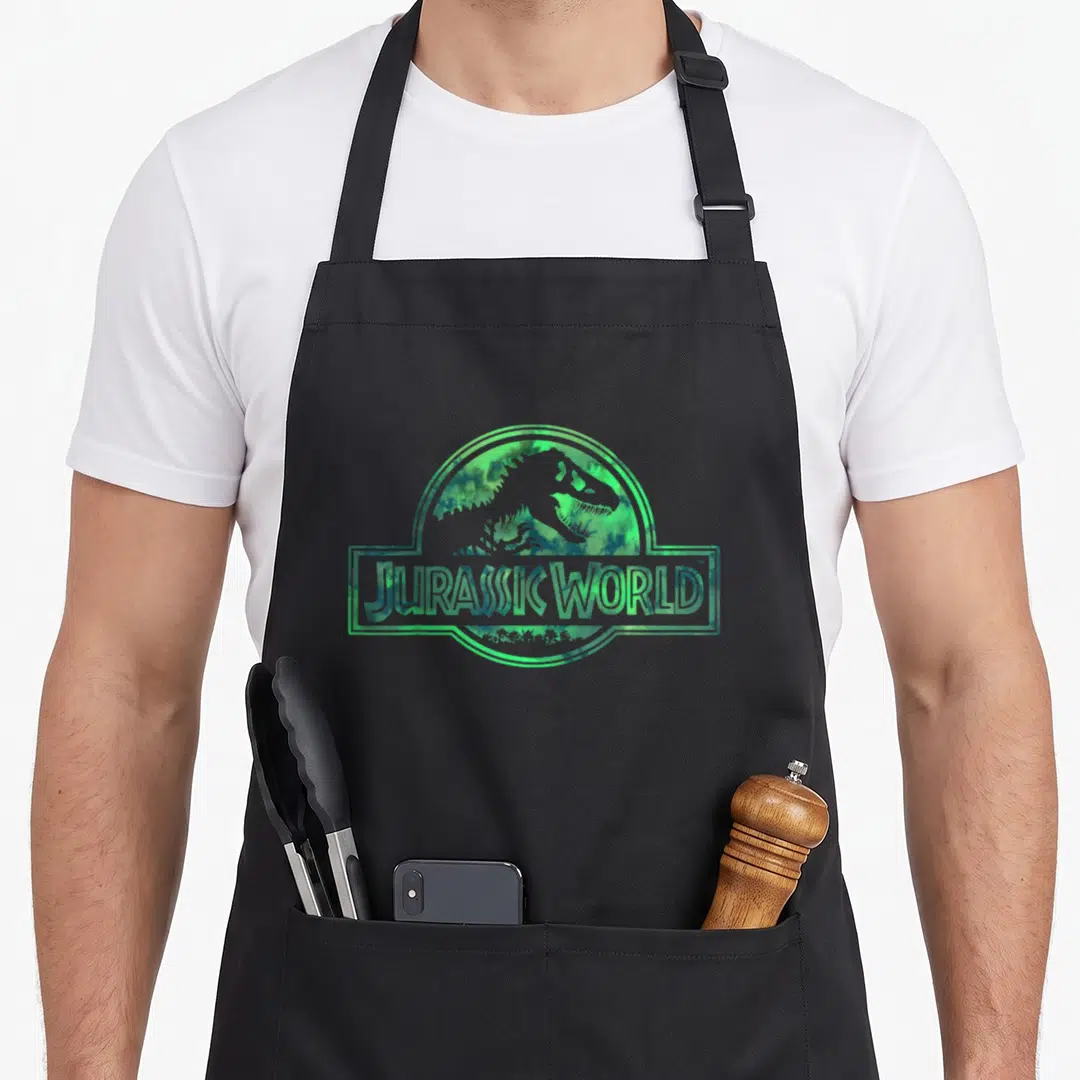 Jurassic watercolor apron - Dinosaur silhouette inside circle and rectangle with JURASSIC WORLD text in green watercolor — shown on a black cotton canvas apron against a white background