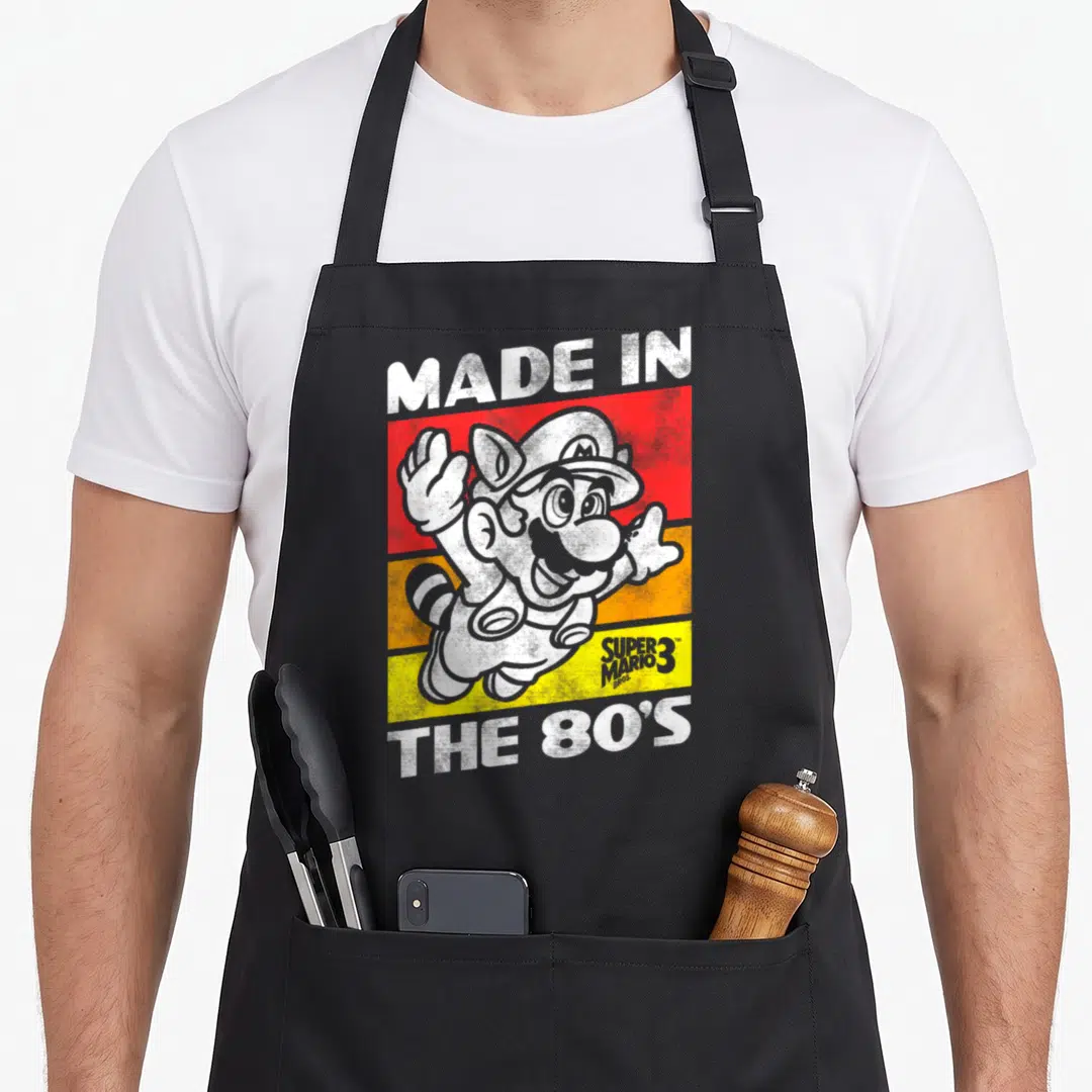 80s holiday apron - Cat Mario character over red orange and yellow stripes with retro text — shown on a black cotton canvas apron against a white background