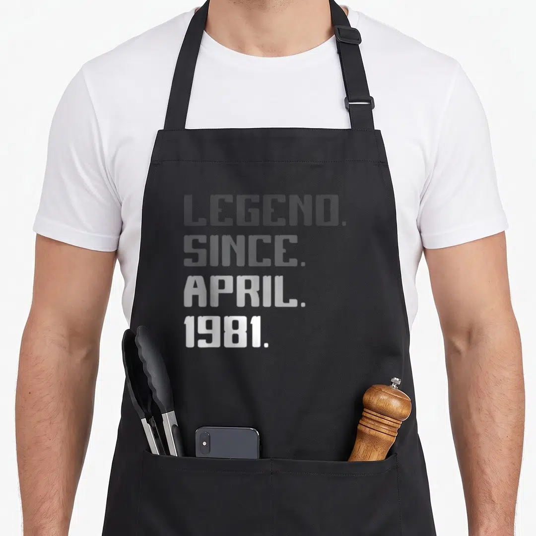 Legend april apron - Stacked white text reading LEGEND SINCE APRIL 1981 on grey background — shown on a black cotton canvas apron against a white background