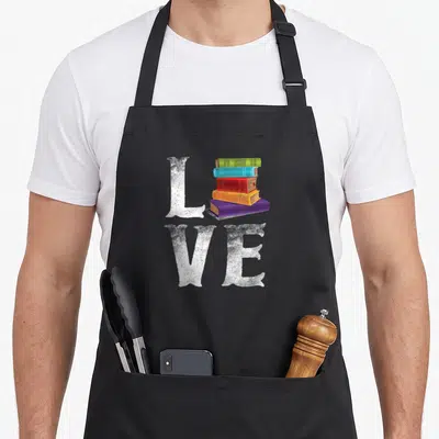 Reading food aprons - Stack of five colored books forming the word LOVE with distressed white letters — shown on a black cotton canvas apron against a white background