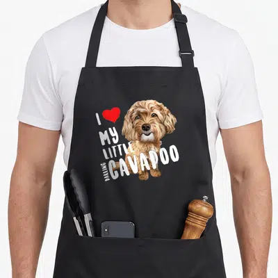 Darling dog apron - Realistic brown and white Cavapoo head with red heart and I love my little darling Cavapoo text — shown on a black cotton canvas apron against a white background