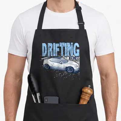 Madness car apron - White car with distressed blue DRIFTING MADNESS text and splatter effects — shown on a black cotton canvas apron against a white background