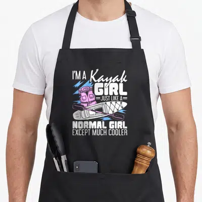Normal kayak girl apron - I'm a Kayak Girl text with pink life jacket and white kayak on blue lightning background — shown on a black cotton canvas apron against a white background