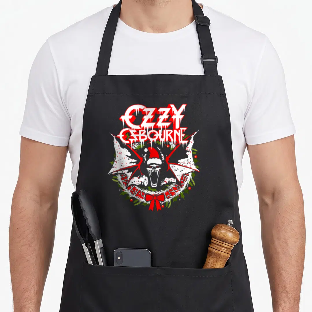 Ozzy holiday apron - Dripping red Ozzy Osbourne text above a screaming bat in a Santa hat inside a green wreath — shown on a black cotton canvas apron against a white background