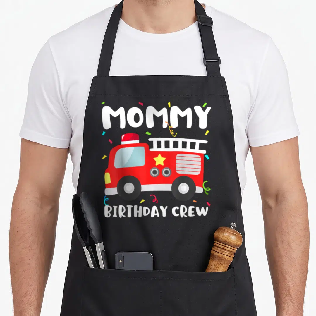 Crew truck apron - Red fire truck with MOMMY BIRTHDAY CREW text and confetti — shown on a black cotton canvas apron against a white background