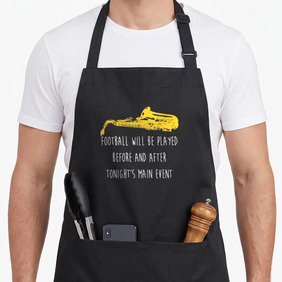 Saxophone football apron - Yellow distressed saxophone above three lines of white text reading FOOTBALL WILL BE PLAYED — shown on a black cotton canvas apron against a white background