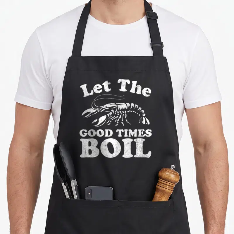 Mardi cajun aprons - White distressed lobster with Let The GOOD TIMES BOIL text — shown on a black cotton canvas apron against a white background