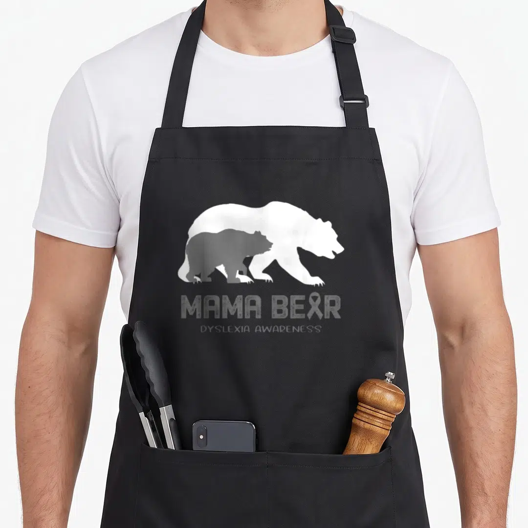 Dyslexia mama bear apron - White and grey bear silhouettes with MAMA BEAR text and ribbon in R — shown on a black cotton canvas apron against a white background