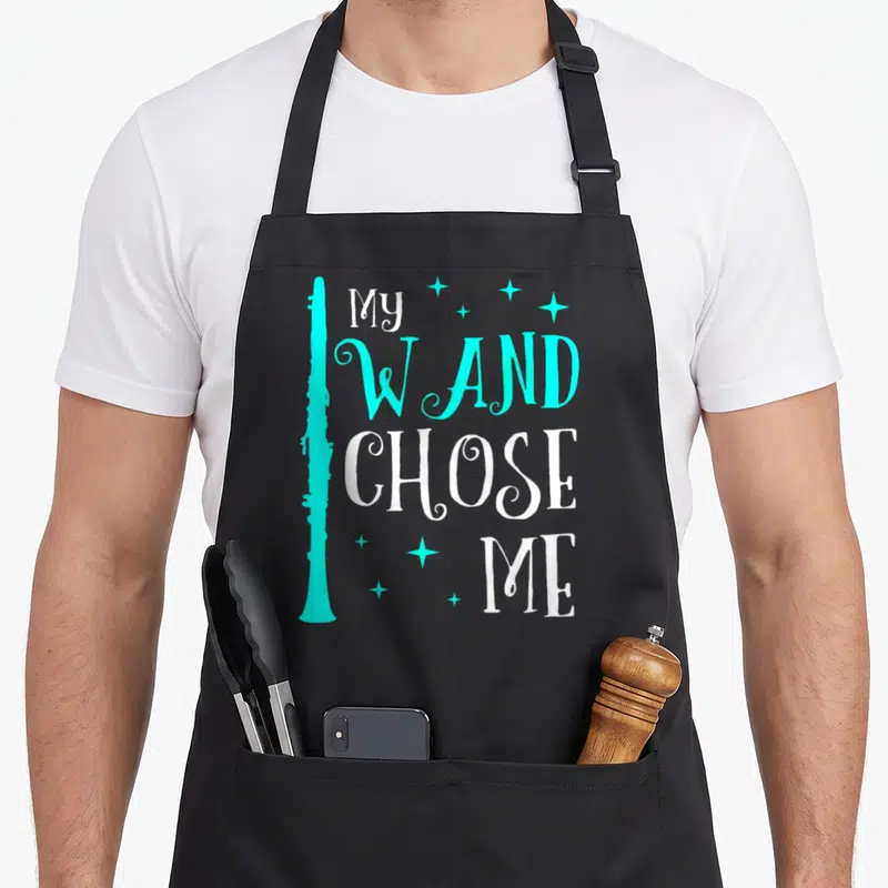 Chose clarinet apron - Cyan clarinet silhouette beside stacked white and cyan text reading my wand chose me with small — shown on a black cotton canvas apron against a white background