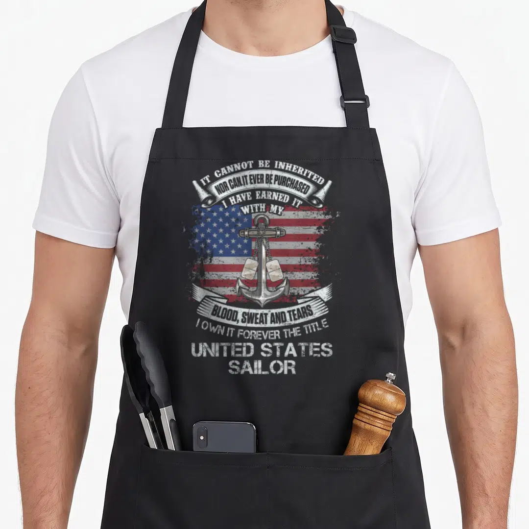 Forever military apron - Silver anchor on distressed flag with text about earning the title of United States Sailor — shown on a black cotton canvas apron against a white background