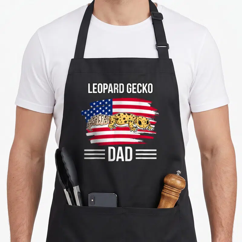 4th leopard apron - Cartoon leopard gecko on red white blue flag with LEOPARD GECKO DAD text — shown on a black cotton canvas apron against a white background