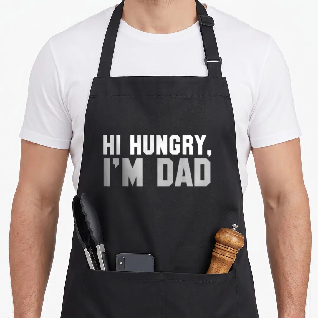 Hungry joke apron - White stacked text reading HI HUNGRY I'M DAD on grey background — shown on a black cotton canvas apron against a white background