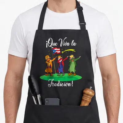Los christmas apron - Three kings dabbing on green grass with Puerto Rican flag and white script text — shown on a black cotton canvas apron against a white background