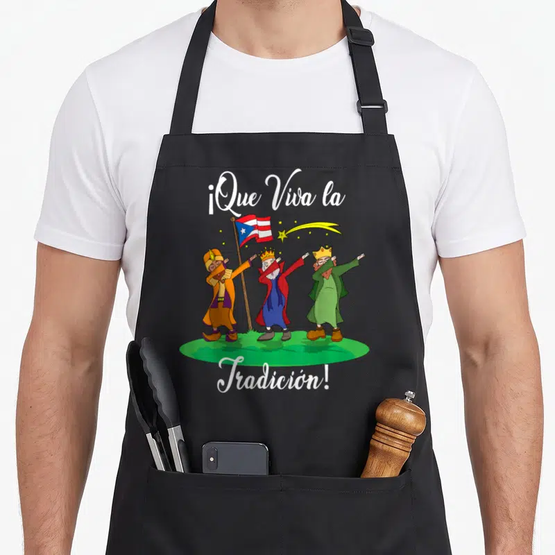 Los christmas apron - Three kings dabbing on green grass with Puerto Rican flag and white script text — shown on a black cotton canvas apron against a white background
