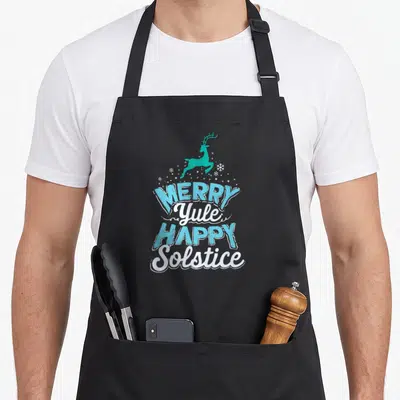 Merry yule winter apron - Teal leaping reindeer above MERRY Yule HAPPY Solstice text in light blue and white — shown on a black cotton canvas apron against a white background