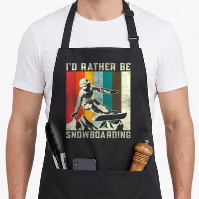 Mountain boarding apron - Retro snowboarder on vertical stripes with I'D RATHER BE SNOWBOARDING text — shown on a black cotton canvas apron against a white background
