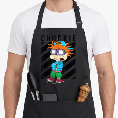 Taping baseball apron - Cartoon character Chuckie with orange hair and glasses standing before diagonal black and grey — shown on a black cotton canvas apron against a white background