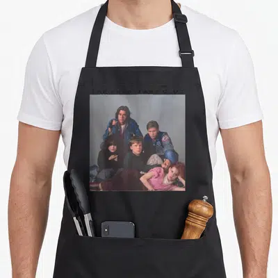 Breakfast century club apron - THE BREAKFAST CLUB text above photo of five teenagers in blue pink green and black — shown on a black cotton canvas apron against a white background