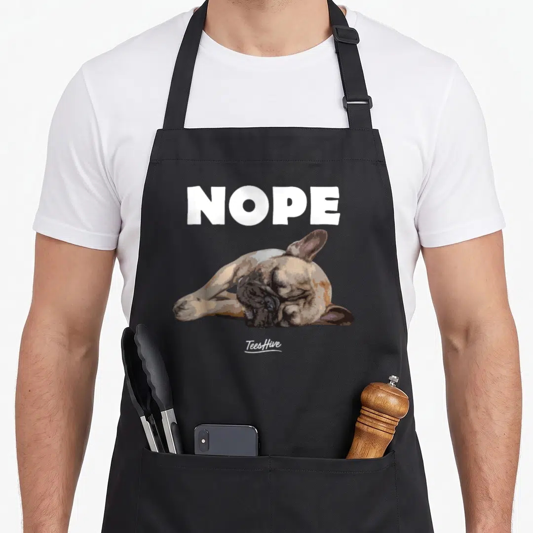 Themed french bulldog apron - NOPE text above a realistic dog lying flat in white, tan, and brown — shown on a black cotton canvas apron against a white background