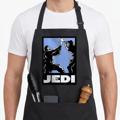 Episode final apron - Two black silhouettes fighting with lightsabers on blue background with JEDI text below — shown on a black cotton canvas apron against a white background