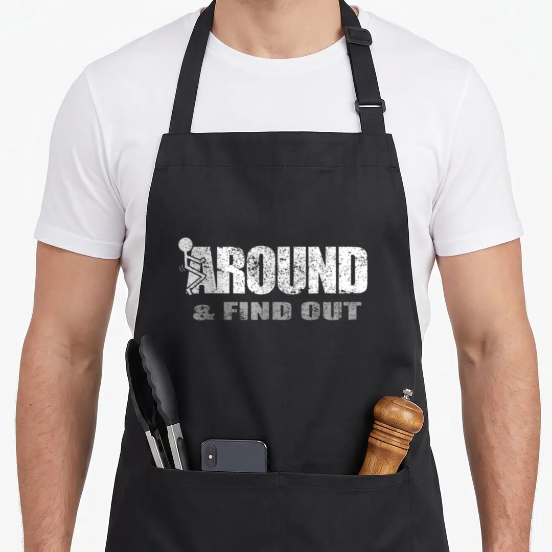 Funny around find aprons for grilling - White AROUND & FIND OUT text with fighting stick figure on black fabric — shown on a black cotton canvas apron against a white background