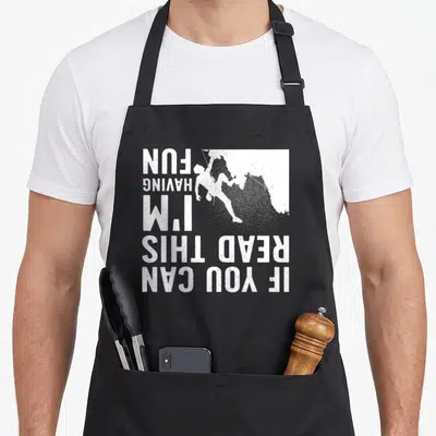 Climbing mountain bouldering apron - Upside down white text reading IF YOU CAN READ THIS I'M HAVING FUN beside a rock — shown on a black cotton canvas apron against a white background