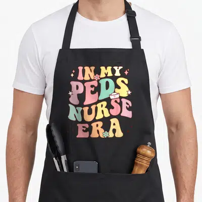 Era nurse apron - Retro stacked text In My PEDS Nurse Era with nurse hat and stars — shown on a black cotton canvas apron against a white background