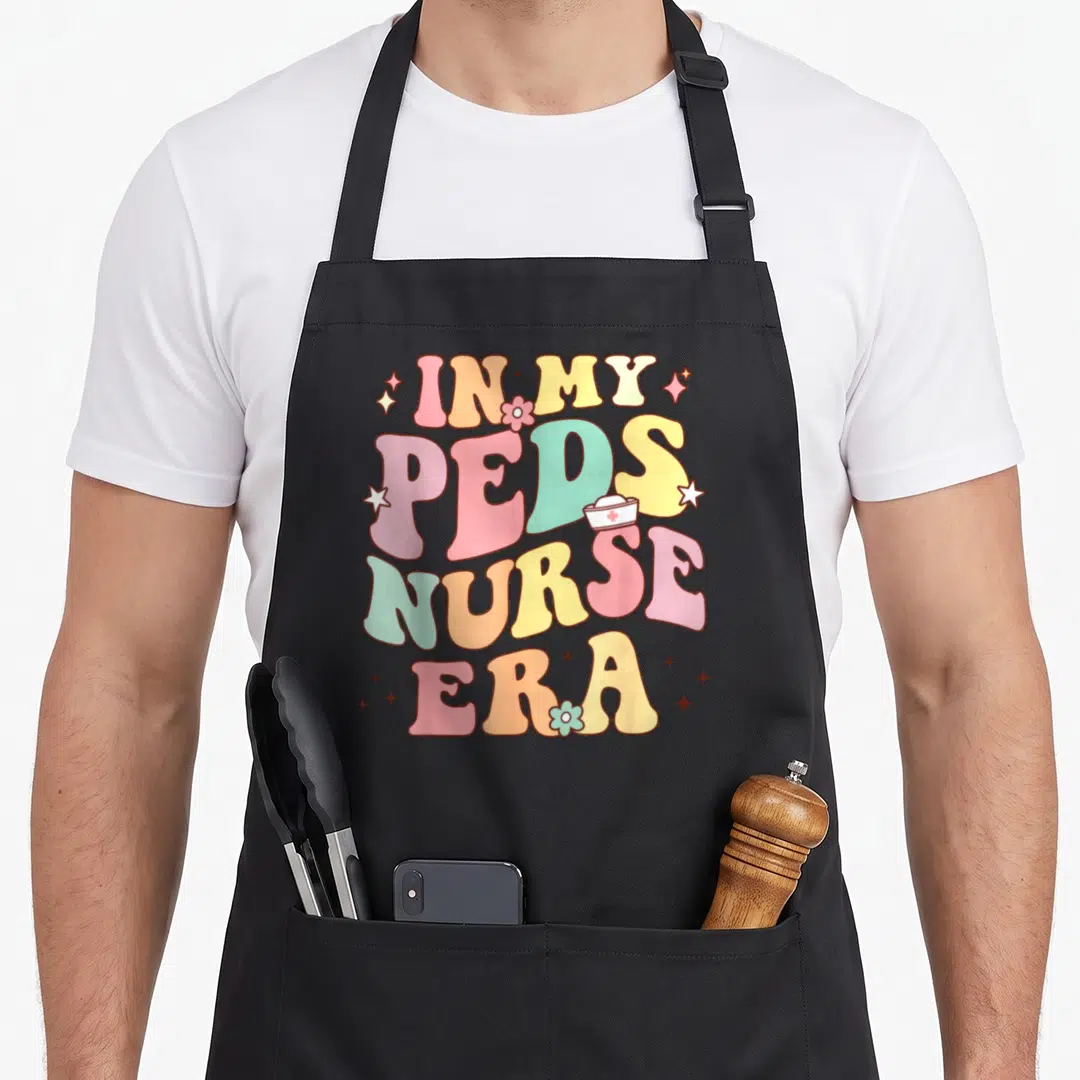 Era nurse apron - Retro stacked text In My PEDS Nurse Era with nurse hat and stars — shown on a black cotton canvas apron against a white background
