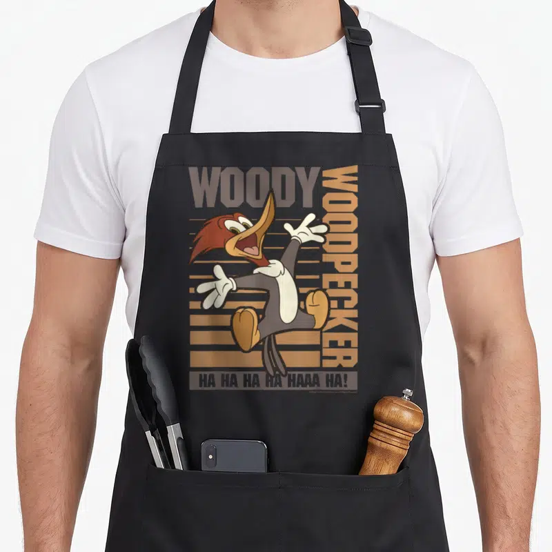 Jumping woodpecker apron - Cartoon woodpecker jumping with WOODY text and brown stripes — shown on a black cotton canvas apron against a white background