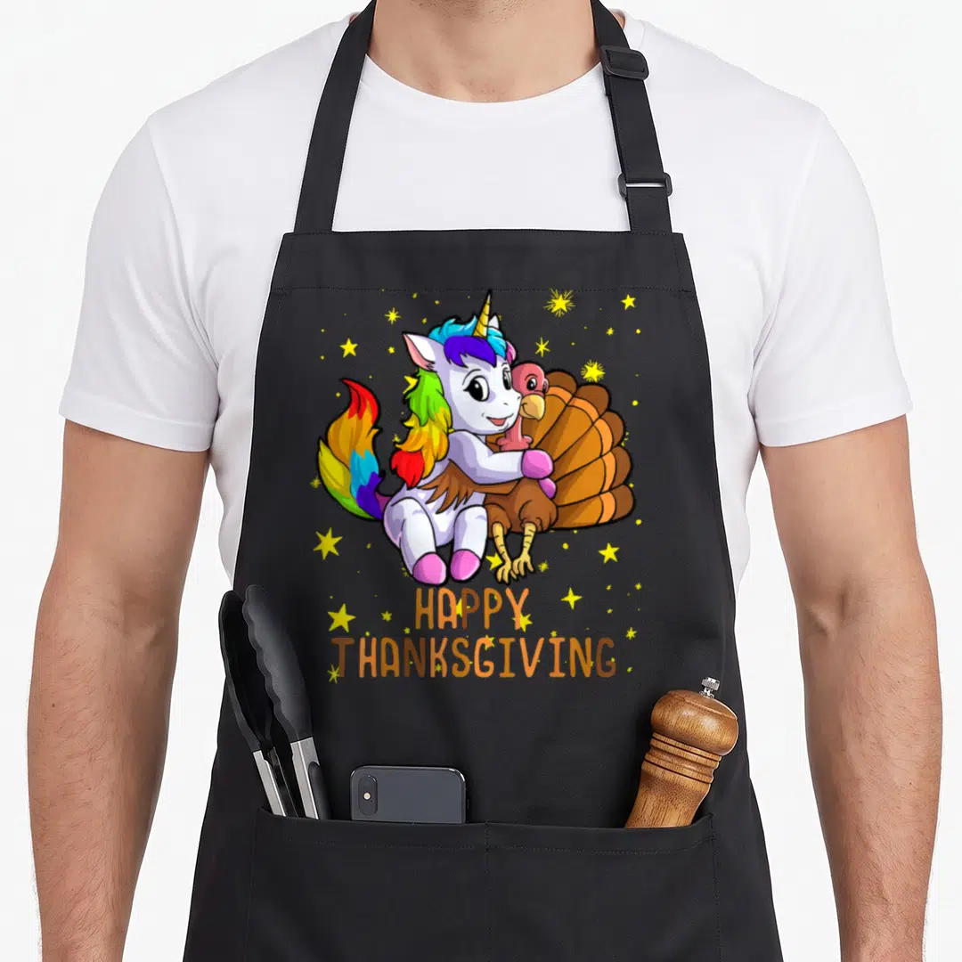 Unicorn thanksgiving apron - Cartoon white unicorn hugging brown turkey with HAPPY THANKSGIVING text and yellow stars — shown on a black cotton canvas apron against a white background