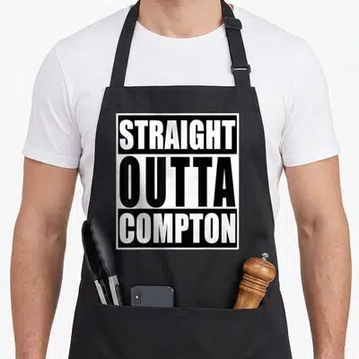 Straight compton apron - Stacked black and white text reading STRAIGHT OUTTA COMPTON inside a square border — shown on a black cotton canvas apron against a white background