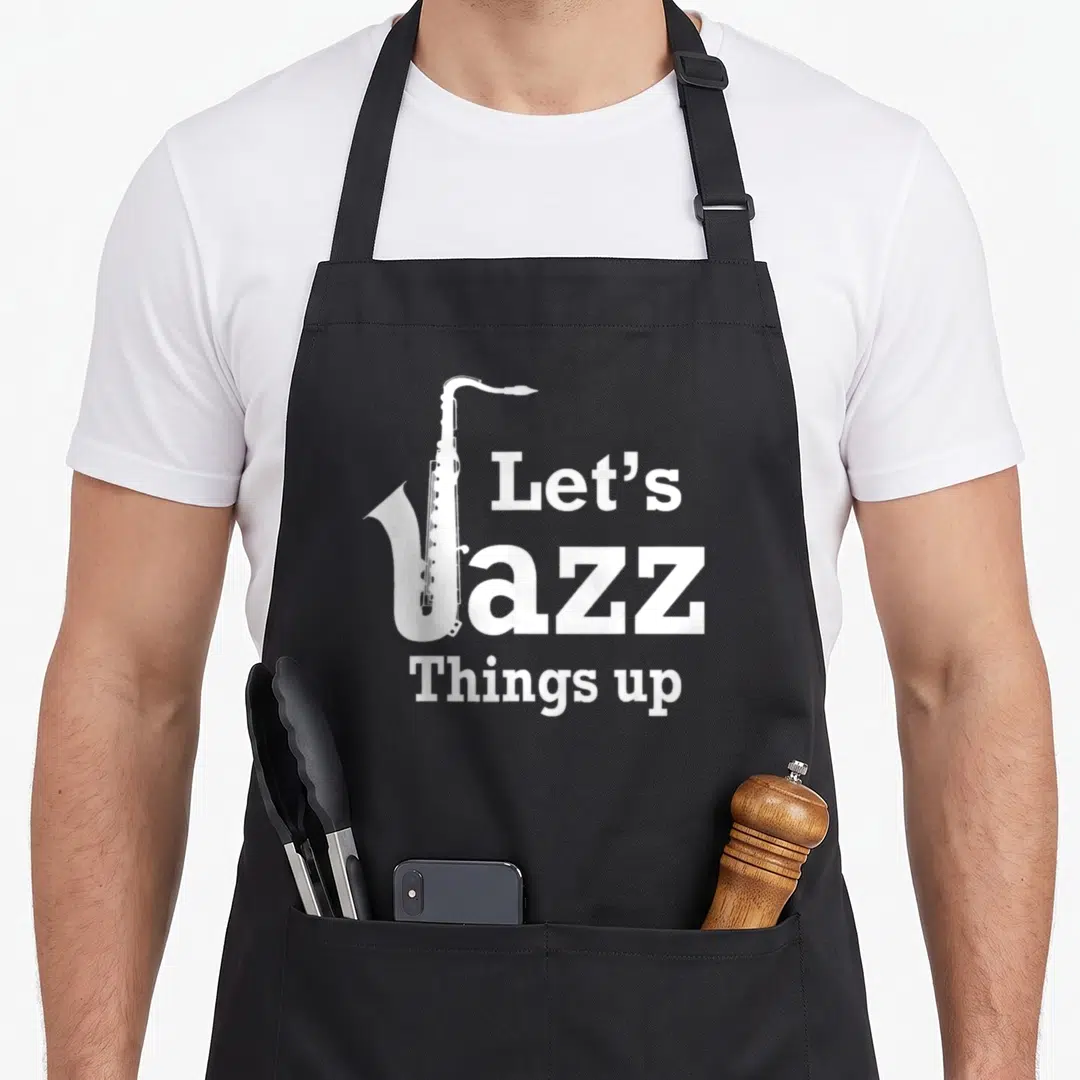 Funny jazz apron - White saxophone graphic overlapping the letter J in stacked Let's Jazz Things up text — shown on a black cotton canvas apron against a white background