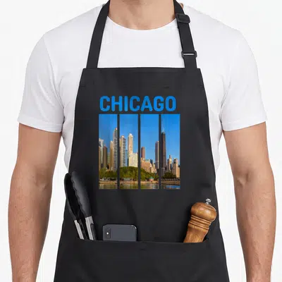 Downtown chicago apron - Blue CHICAGO text above four vertical photo panels of the skyline showing buildings and green — shown on a black cotton canvas apron against a white background