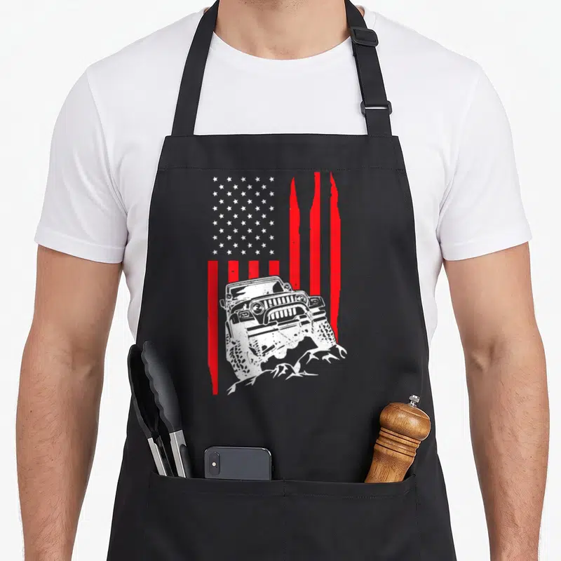 Crawler american flag apron - White off-road vehicle climbing rocks over distressed red and white flag stripes — shown on a black cotton canvas apron against a white background