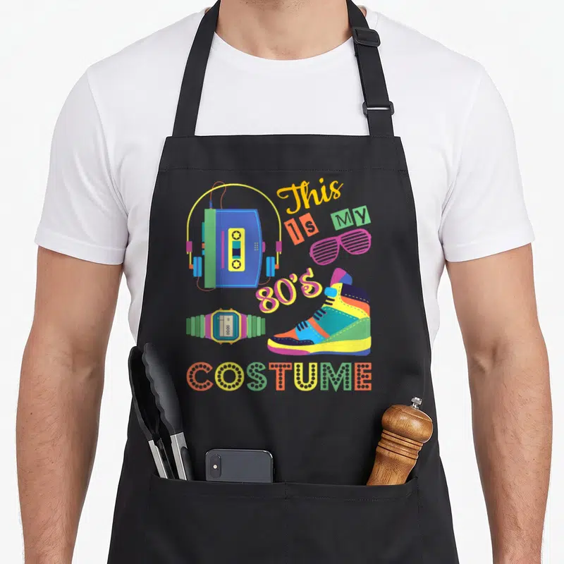 Cute costume 80s apron - Colorful cartoon boombox sneaker watch and glasses with This Is My 80s Costume text — shown on a black cotton canvas apron against a white background