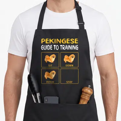 Pekingese dog training apron - Pekingese dog cartoon with sit down fetch images and empty stay box — shown on a black cotton canvas apron against a white background