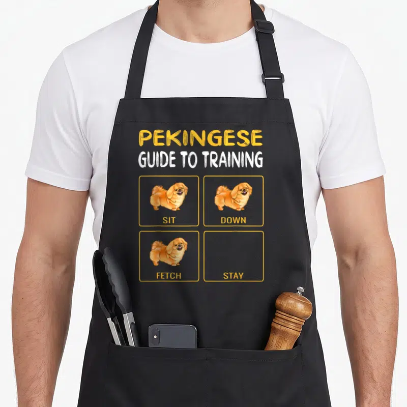 Pekingese dog training apron - Pekingese dog cartoon with sit down fetch images and empty stay box — shown on a black cotton canvas apron against a white background
