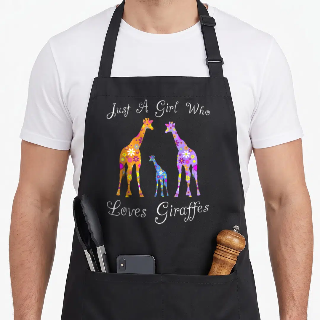 Cute giraffe apron - Three floral giraffes in orange, purple, and blue with white text reading Just A Girl Who Loves — shown on a black cotton canvas apron against a white background