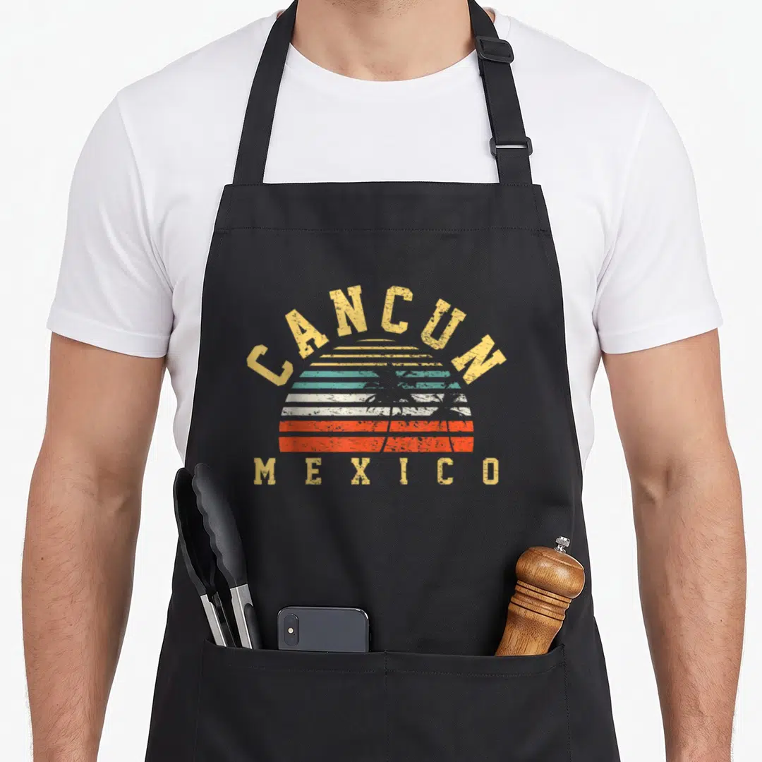 Funny cancun mexico apron - Retro striped sun graphic with CANCUN and MEXICO text in yellow teal orange white — shown on a black cotton canvas apron against a white background