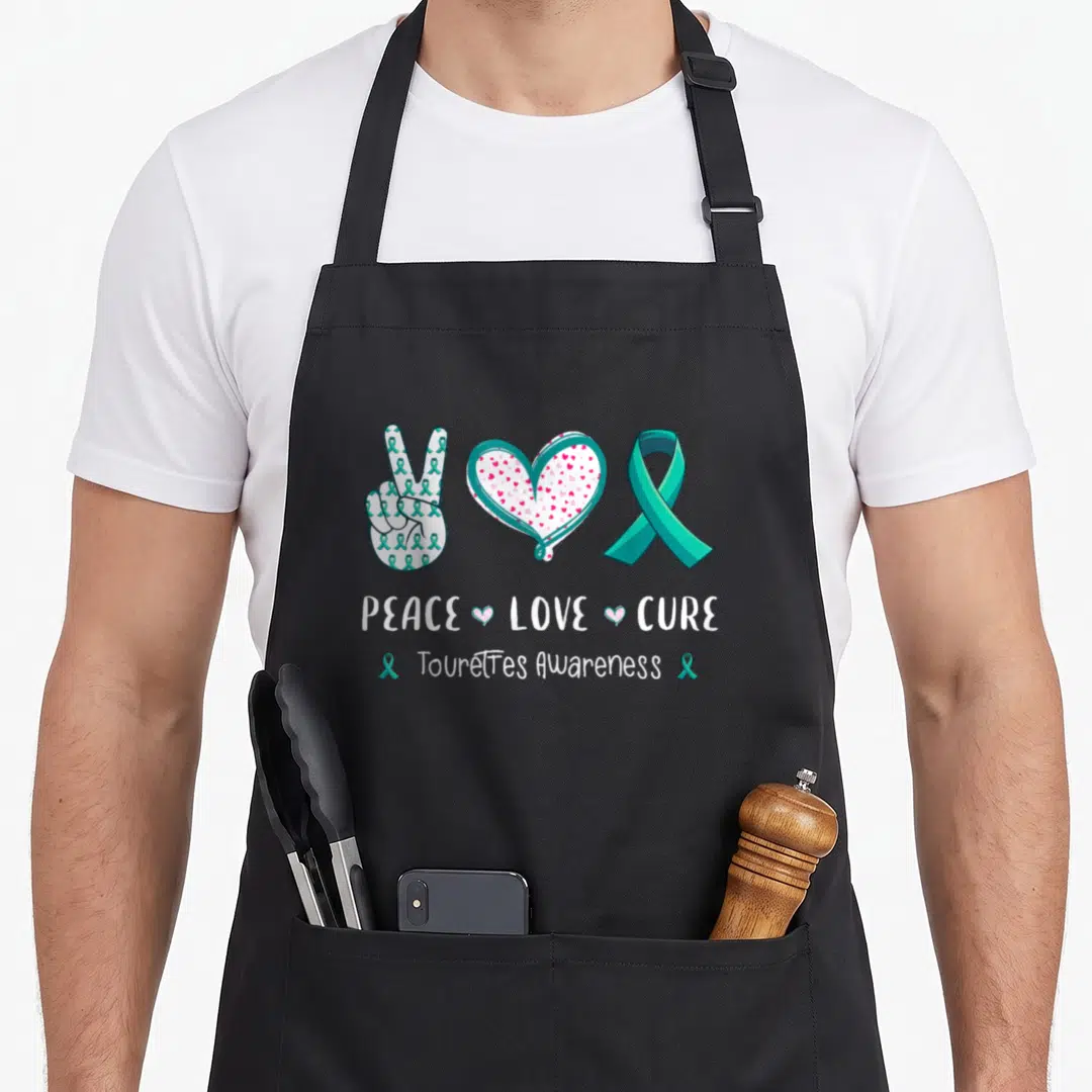 Peace tourette awareness apron - Teal peace sign, pink heart, teal ribbon above PEACE LOVE CURE text — shown on a black cotton canvas apron against a white background