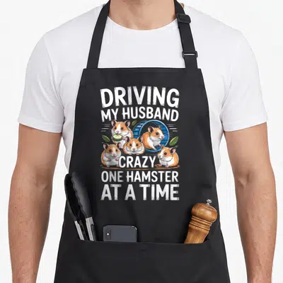 Hamster driving apron - Four cartoon hamsters with cucumber and wheel under white text — shown on a black cotton canvas apron against a white background