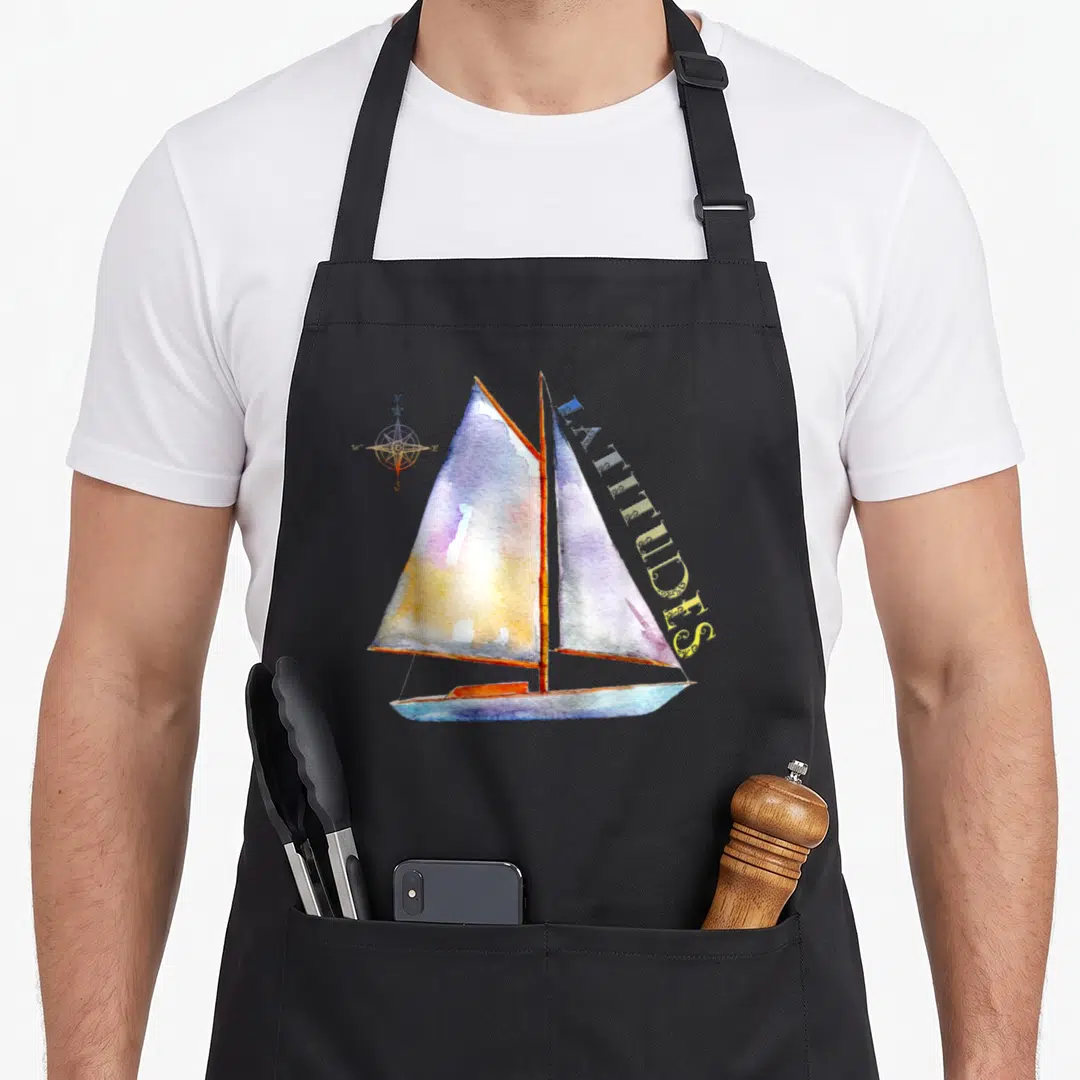 Watercolor houseboat apron - Watercolor sailboat with vertical LATITUDES text and compass in blue purple yellow orange — shown on a black cotton canvas apron against a white background