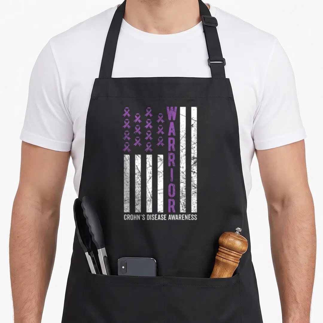 Funny warrior crohns awareness apron - Purple ribbons and white stripes with vertical WARRIOR text and distressed — shown on a black cotton canvas apron against a white background