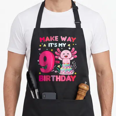 Retro axolotl birthday apron - Pink axolotl number 9 cake cartoon withMAKE WAY IT'S MY 9TH BIRTHDAY text — shown on a black cotton canvas apron against a white background