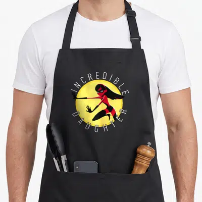 Incredible mom daughter aprons - Superhero girl in red suit inside yellow circle with white text INCREDIBLE DAUGHTER — shown on a black cotton canvas apron against a white background