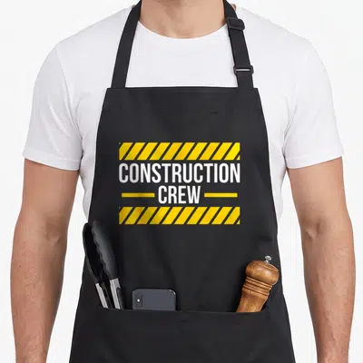 Construction road apron - CONSTRUCTION CREW text between yellow and grey hazard stripes on grey background — shown on a black cotton canvas apron against a white background