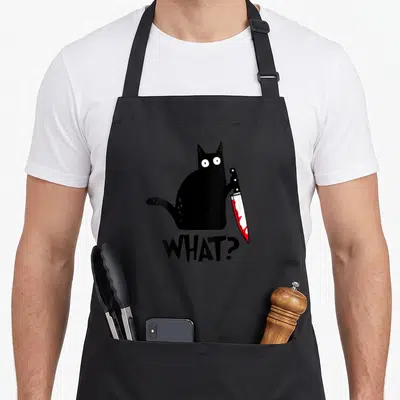 Cute murderous black cat apron - Cartoon black cat holding a knife with red blood above the word WHAT? — shown on a black cotton canvas apron against a white background
