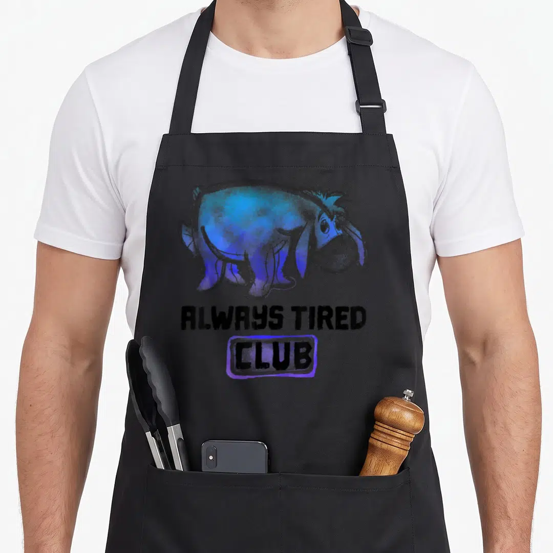 Alway eeyore apron - Blue cartoon donkey with stitched tail above black text ALWAYS TIRED CLUB in purple box — shown on a black cotton canvas apron against a white background