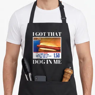 Meme dog apron - Retro hot dog and soda ad with I GOT THAT DOG IN ME text and 1.50 price tag — shown on a black cotton canvas apron against a white background