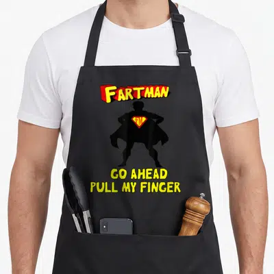 Fart pull girl apron - Fartman superhero silhouette with Go Ahead Pull My Finger text in red and yellow — shown on a black cotton canvas apron against a white background